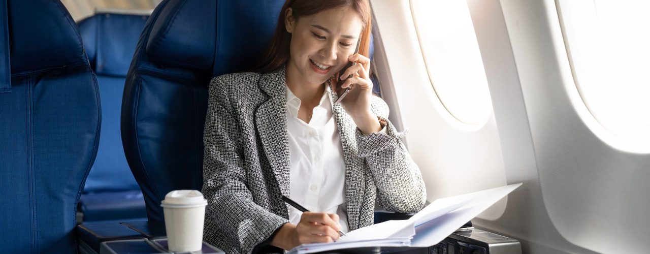 Business young asian woman talking on phone during working for paperwork financial report on airplane, flight in plane.